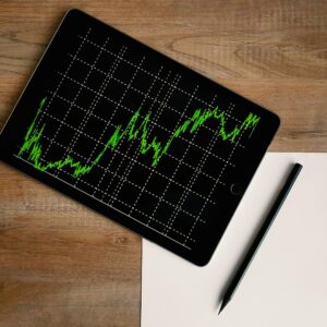 Flatlay of an iPad displaying stock market graph on a wooden desk with a pencil and paper.